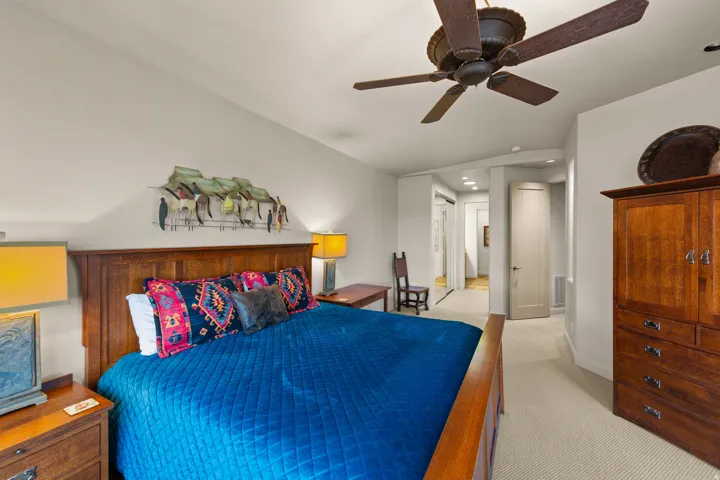 Vaulted ceiling with an integrated ceiling fan, light neutral wall paint, wood-finish bed frame, light neutral carpet flooring, and a solid-core interior door