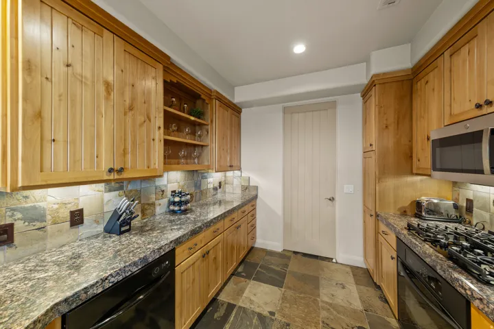 Warm wood cabinetry, stone tile flooring, and integrated stainless steel appliances