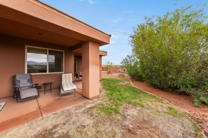 Covered patio with a concrete surface, large exterior window, and mature landscaping