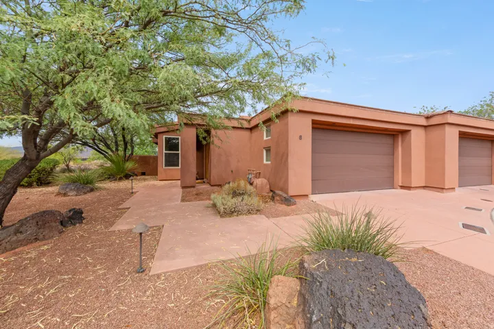 Stucco exterior with multiple garage doors, concrete pathway, and desert landscaping