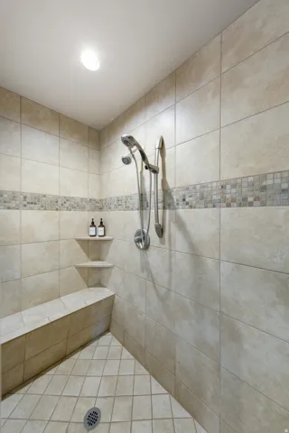 Tiled shower featuring a built-in bench, recessed shelves, mosaic accent tile, and a handheld shower fixture