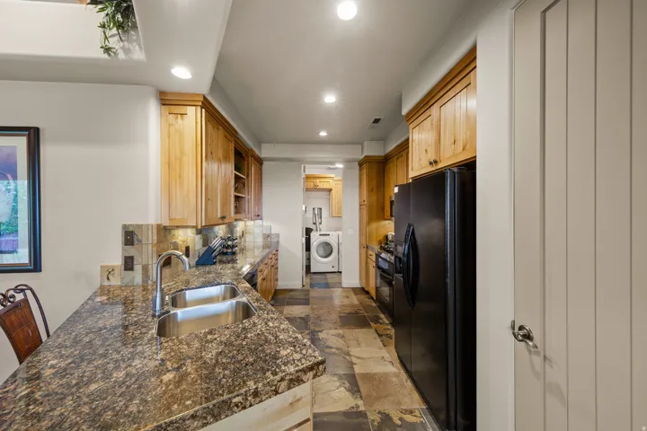 Kitchen featuring wood cabinetry, stone-finish countertops, stainless steel double-basin sink, and a stone-look tile backsplash