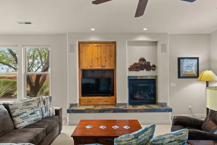 Built-in entertainment center with wood-finish cabinetry, integrated fireplace with stone-tile surround, dual windows, and recessed lighting