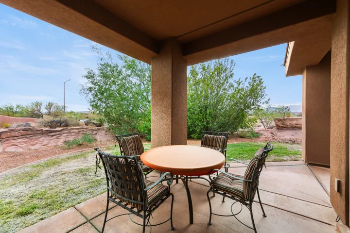 Covered patio with a concrete slab, framed by desert landscaping and mature greenery