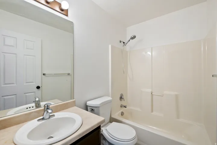 White bathroom featuring a single vanity, integrated sink, chrome faucet, and a combination shower and tub with a white surround
