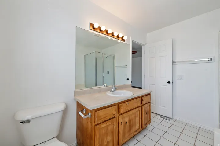 Bathroom featuring a wood-finish vanity with an integrated sink, a large wall mirror, and overhead vanity lighting