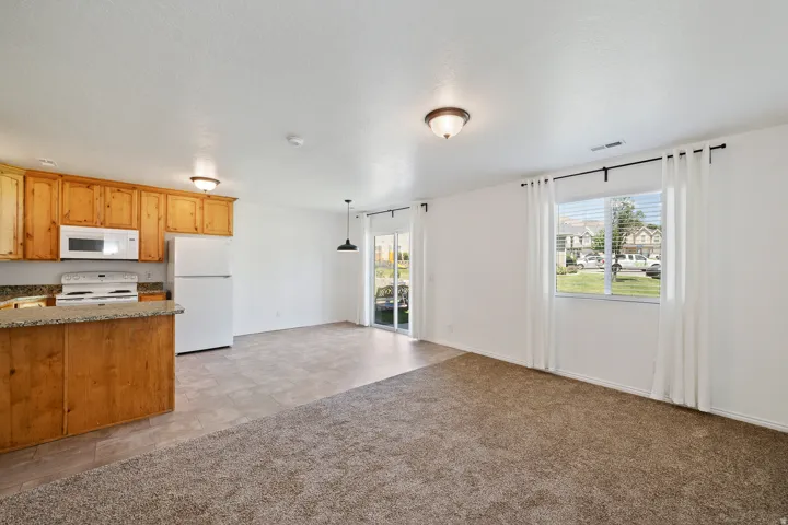 Open-concept living area featuring a kitchen with light wood cabinetry, stone-finish countertops, and white appliances