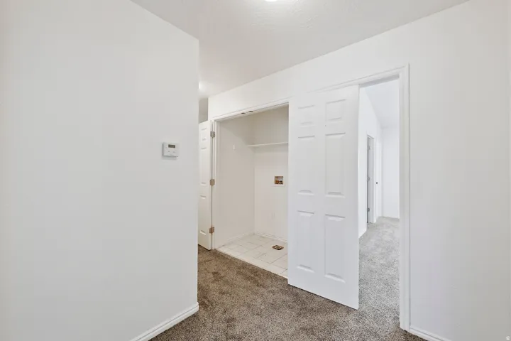 Hallway with carpet flooring, a thermostat, and a utility closet featuring a tiled floor, shelving, and bifold doors