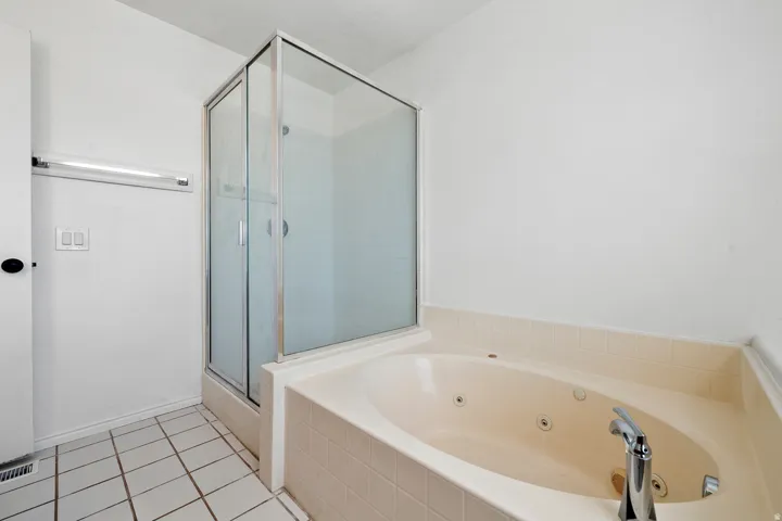 Built-in jetted tub with chrome fixtures, tiled surround, and a glass-enclosed shower