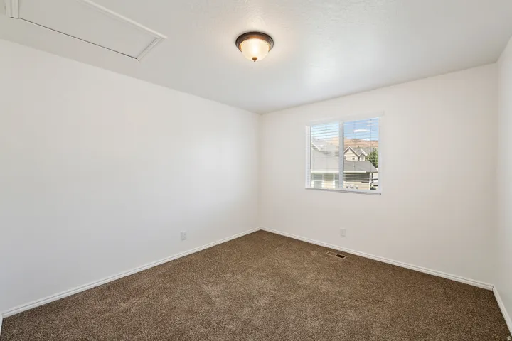 Neutral wall paint with textured carpeting, a single window with horizontal blinds, and a ceiling-mounted light fixture
