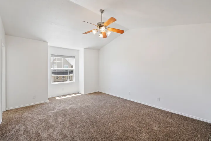 Vaulted ceilings, a ceiling fan with integrated lighting, and a neutral carpeted floor