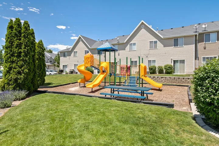 Community recreational area featuring a playground, picnic table, and landscaped green space
