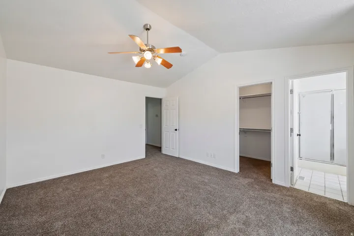 Vaulted ceiling with a ceiling fan, carpet flooring, a walk-in closet with built-in shelving, and an en-suite bathroom with a shower enclosure