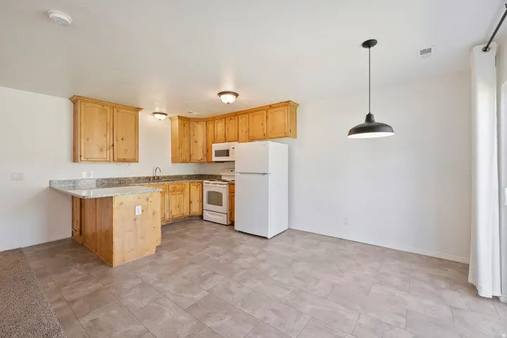 Light wood cabinetry, light-toned granite-style countertops, white appliances, tile flooring, and a pendant light fixture