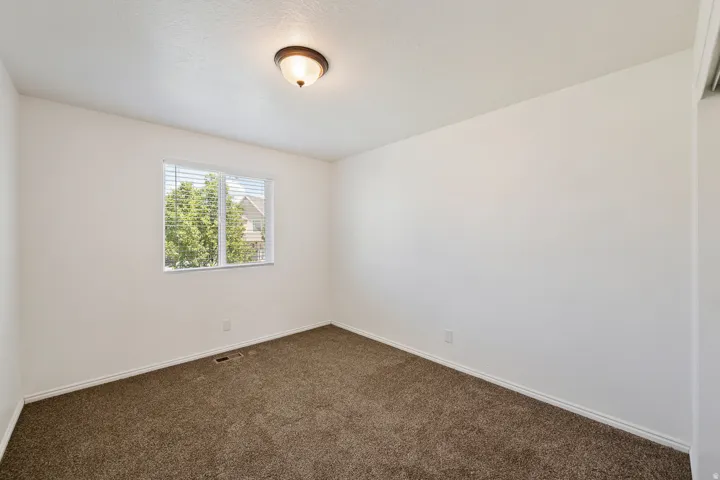Neutral wall color, brown carpet flooring, flush mount ceiling light fixture, window with blinds