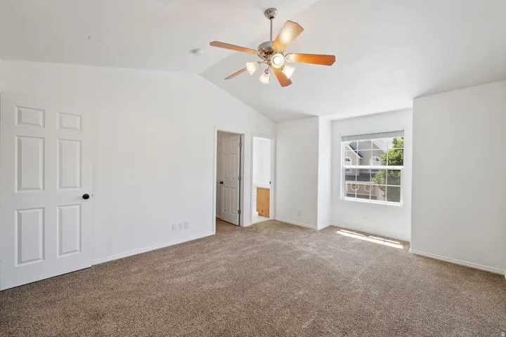 Vaulted ceiling, ceiling fan with integrated lighting, carpeted flooring, paneled interior doors, and a window with blinds