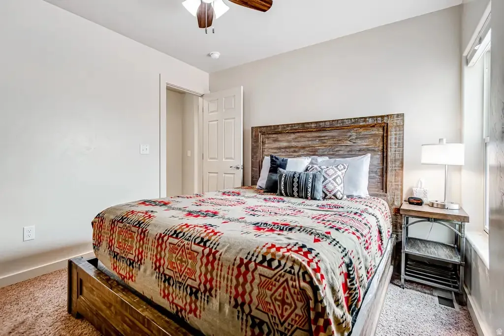 Carpeted bedroom featuring a wooden bed frame with a matching headboard, a ceiling fan, and a window for natural light