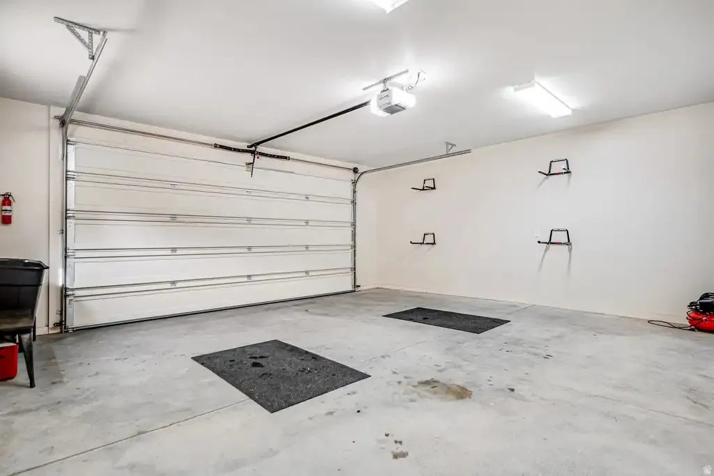 Spacious garage with an automatic overhead door, concrete flooring, and ceiling-mounted lighting