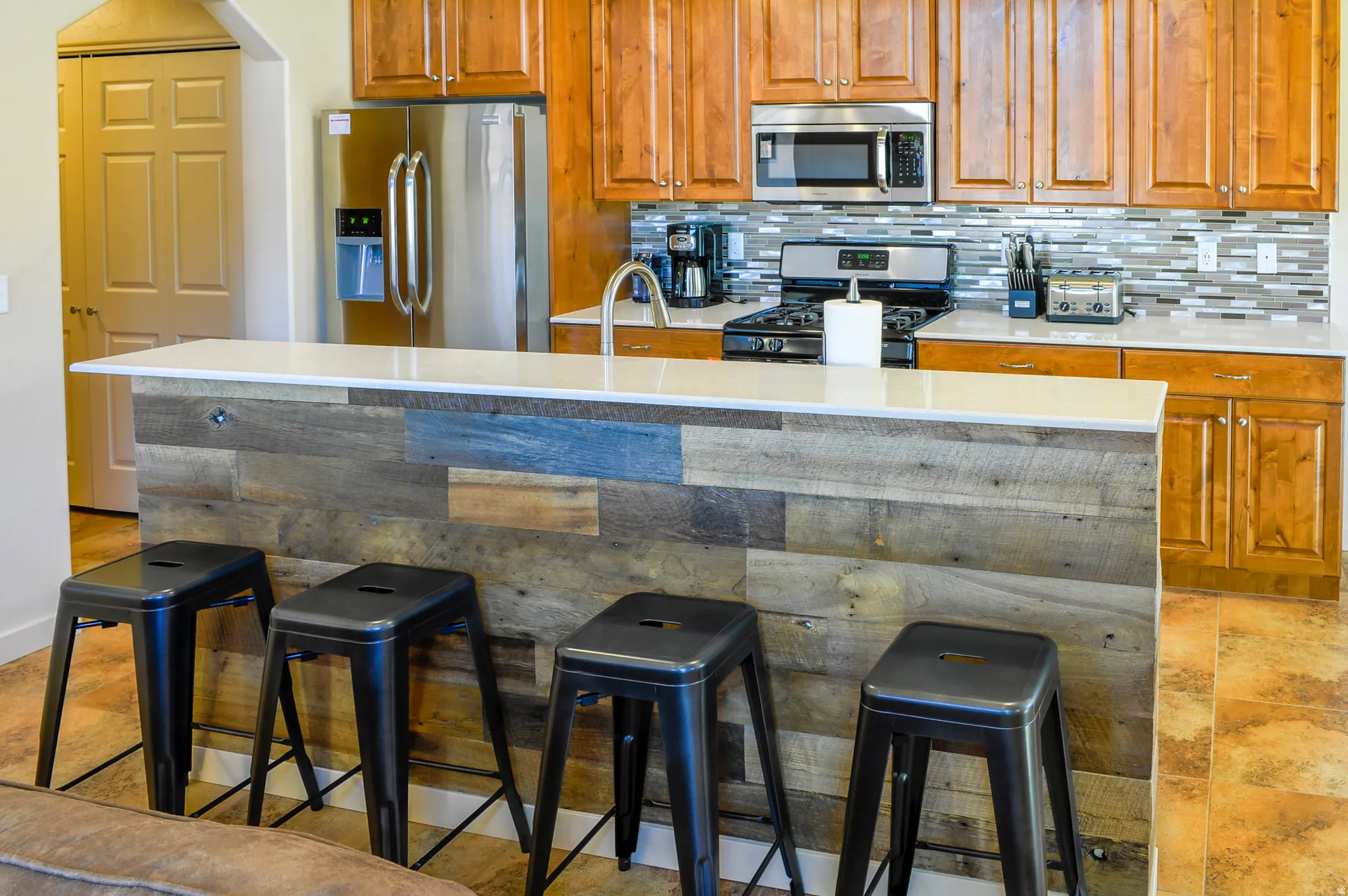Kitchen featuring a breakfast bar with a wood-finish facade, light-toned countertop, and stainless steel appliances