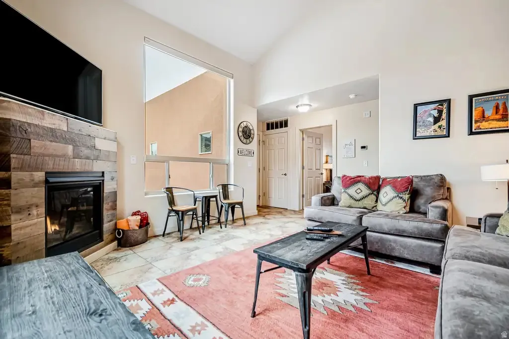 Living area with a wood-clad fireplace, high ceilings, large windows, and tile flooring