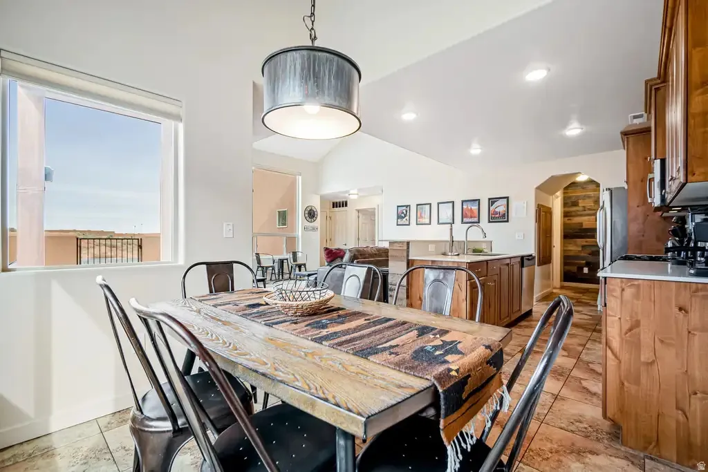 Vaulted ceiling, open concept layout, wood-finish cabinetry, tile flooring, and a large window