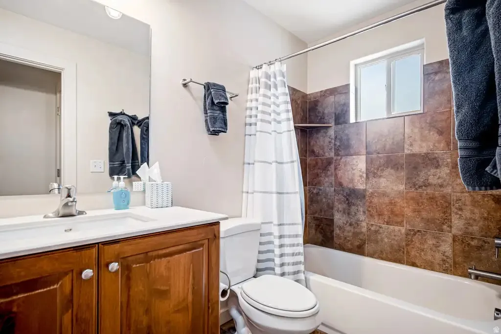 Bathroom featuring a single vanity with wood-finish cabinetry, a drop-in sink, and a built-in bathtub with a tiled surround