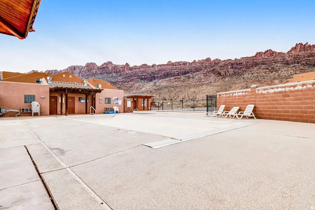 Outdoor pool area with surrounding concrete decking, a low brick wall, and distant rock formations