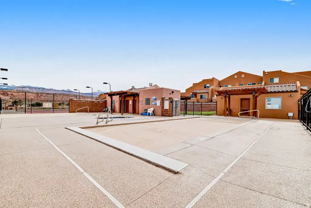 Community pool with integrated hot tub, surrounding paved deck, and adjacent tennis courts