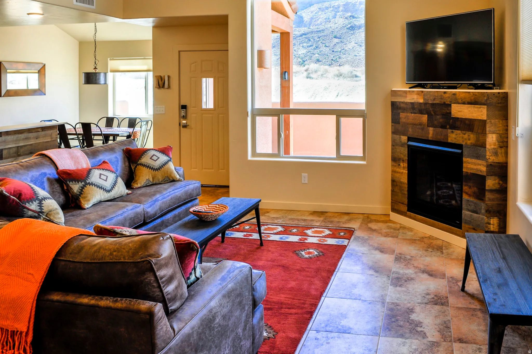 Living area featuring a corner-mounted fireplace with natural stone surround, tile flooring, and a large window