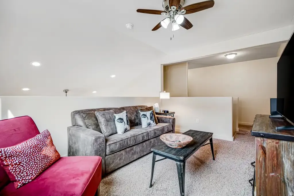Vaulted ceiling with a ceiling fan, recessed lighting, carpet flooring, and a partial wall separation