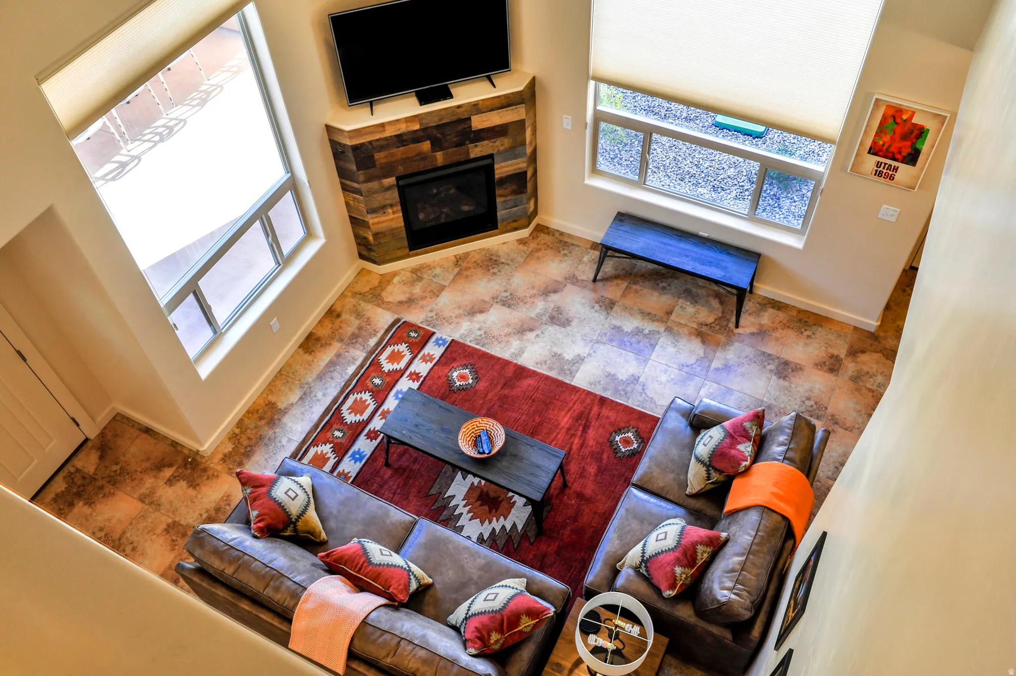 Spacious living area featuring high ceilings, large windows, a corner fireplace with stone surround, and wood-look flooring