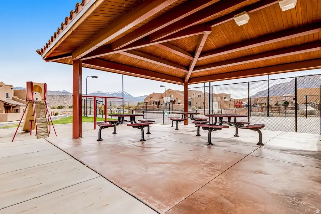 Covered outdoor patio with exposed wood ceiling beams, concrete flooring, and multiple picnic tables
