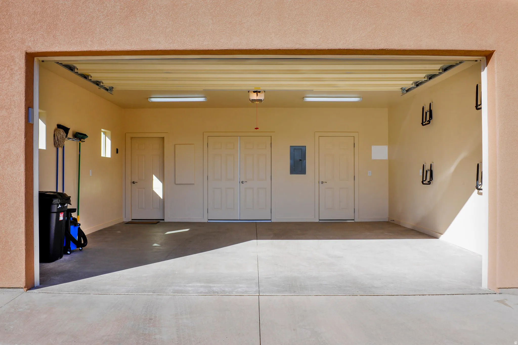 Spacious garage featuring a smooth concrete floor, integrated overhead lighting, multiple access doors, and wall-mounted storage hooks