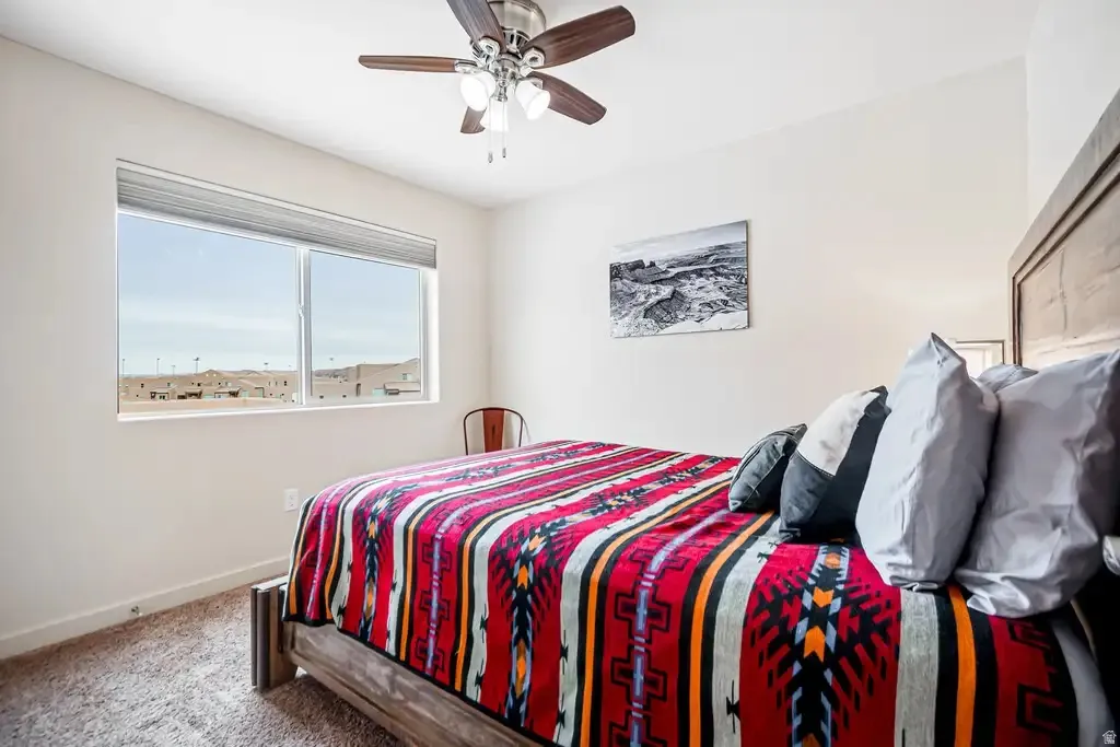Bedroom with carpeted flooring, a ceiling fan with light fixture, and a large window with blinds