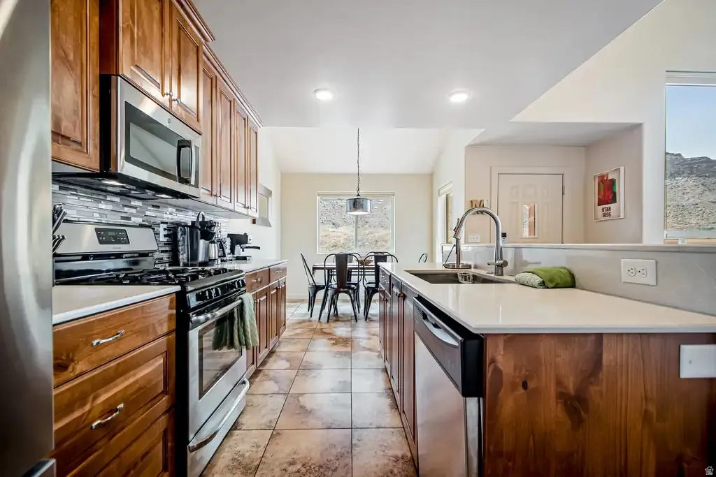 Kitchen featuring wood cabinetry, stainless steel appliances, white countertops, tile flooring, and a tile backsplash