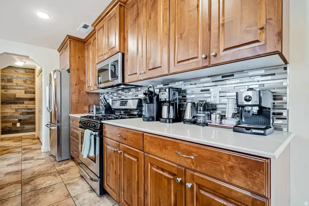 Wood cabinetry with stainless steel hardware, white solid surface countertops, tile backsplash, and stainless steel appliances
