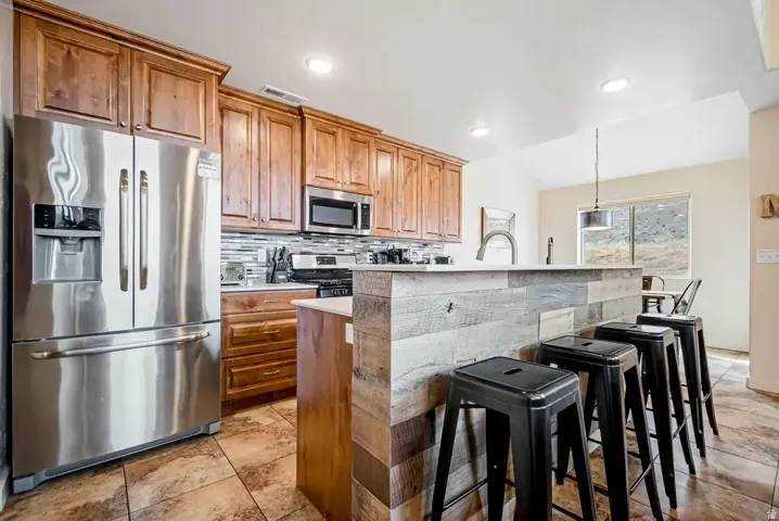 Stainless steel appliances, wood cabinetry, tile flooring, kitchen island with wood paneling, and pendant lighting