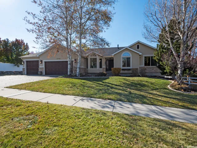 Stucco exterior with stone accents, arched window, two-car garage, mature trees, and a concrete driveway