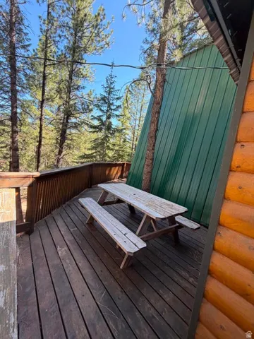 Wood deck with railing, surrounded by mature trees, features a green metal-sided structure