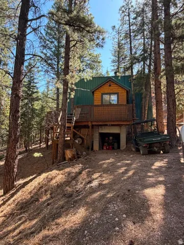 Wood-sided cabin with a green metal roof, elevated on a wooden deck with railing, featuring an integrated ground-level garage