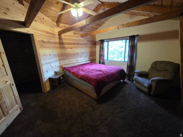 Vaulted wood-paneled ceiling with exposed beams, wood-plank walls, ceiling fan, and carpeted flooring