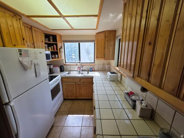 Full wall of wood-finish cabinetry, tile countertops with coordinating backsplash, double basin sink, and tile flooring