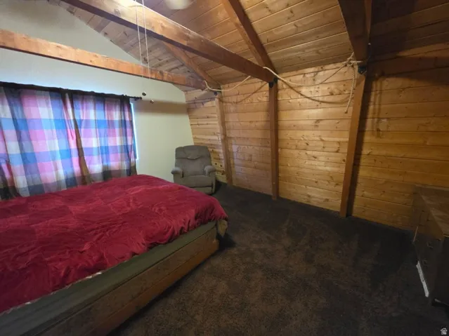 Vaulted wood-paneled ceiling with exposed beams, wood-plank accent wall, and dark carpeting