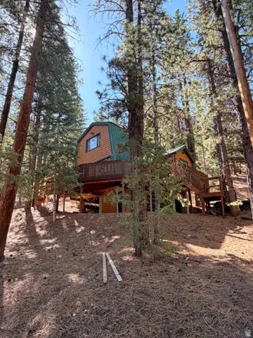 Elevated home with wood siding and a green metal roof, surrounded by mature pine trees