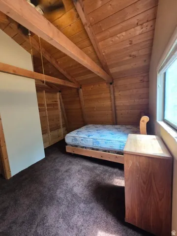Vaulted wood-paneled ceiling with exposed wood beams, wood-paneled walls, and carpeted flooring