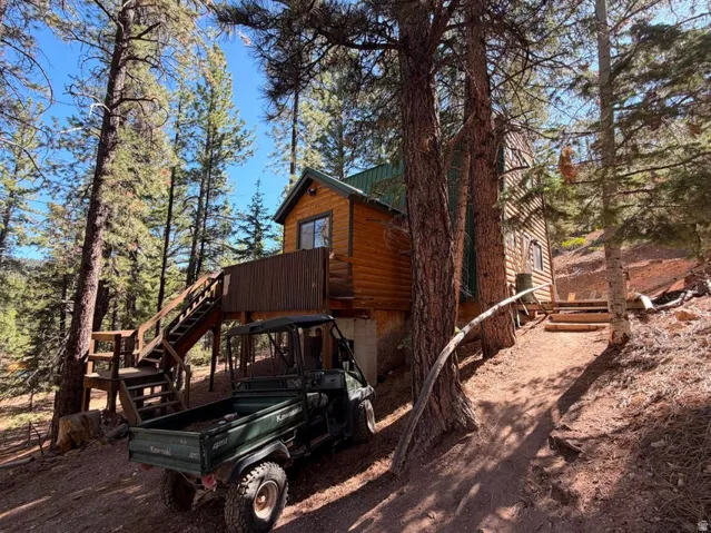 Wood-clad exterior with a dark green metal roof, elevated wood deck with stairs, and multiple mature pine trees