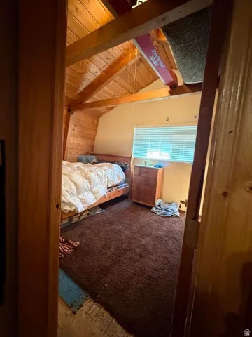 Wood-paneled vaulted ceiling with exposed beams, horizontal window blinds, and carpeting