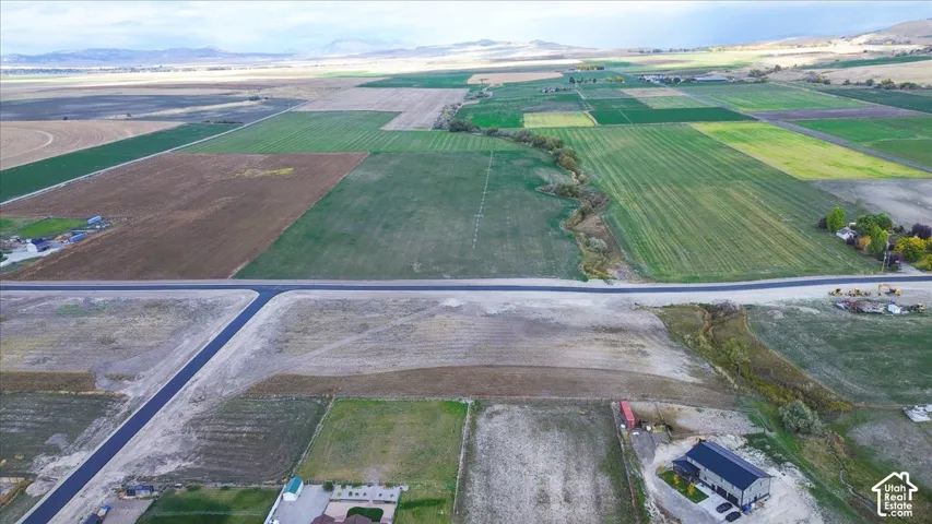 Aerial view of expansive acreage featuring vast open fields, a paved road frontage, and a mountain backdrop