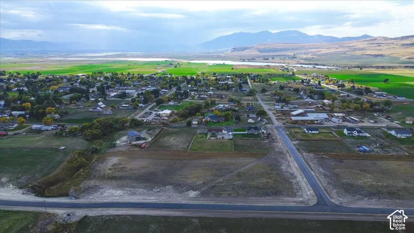 Aerial perspective of expansive rural acreage featuring paved road access, open landscape, and mountain range backdrop