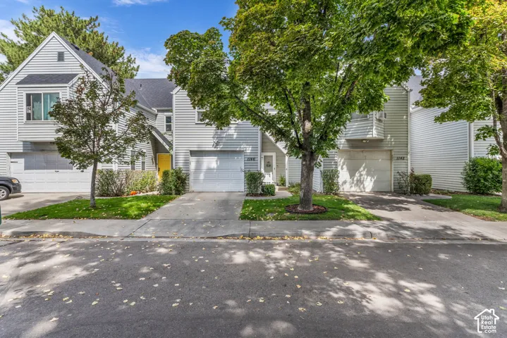 Townhome exterior featuring horizontal siding, attached garage, concrete driveway, and mature landscaping